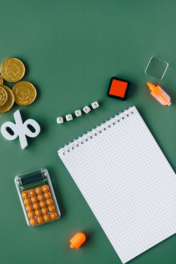 Flat lay of tax-related items on green background including coins, notebook, and calc.